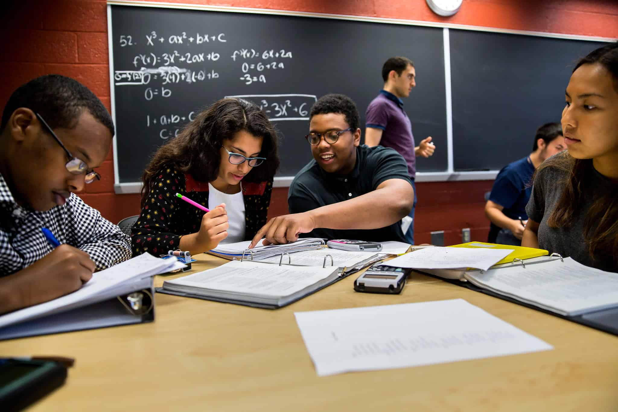 Four students of color work together at a table strewn with notebooks and calculators.
