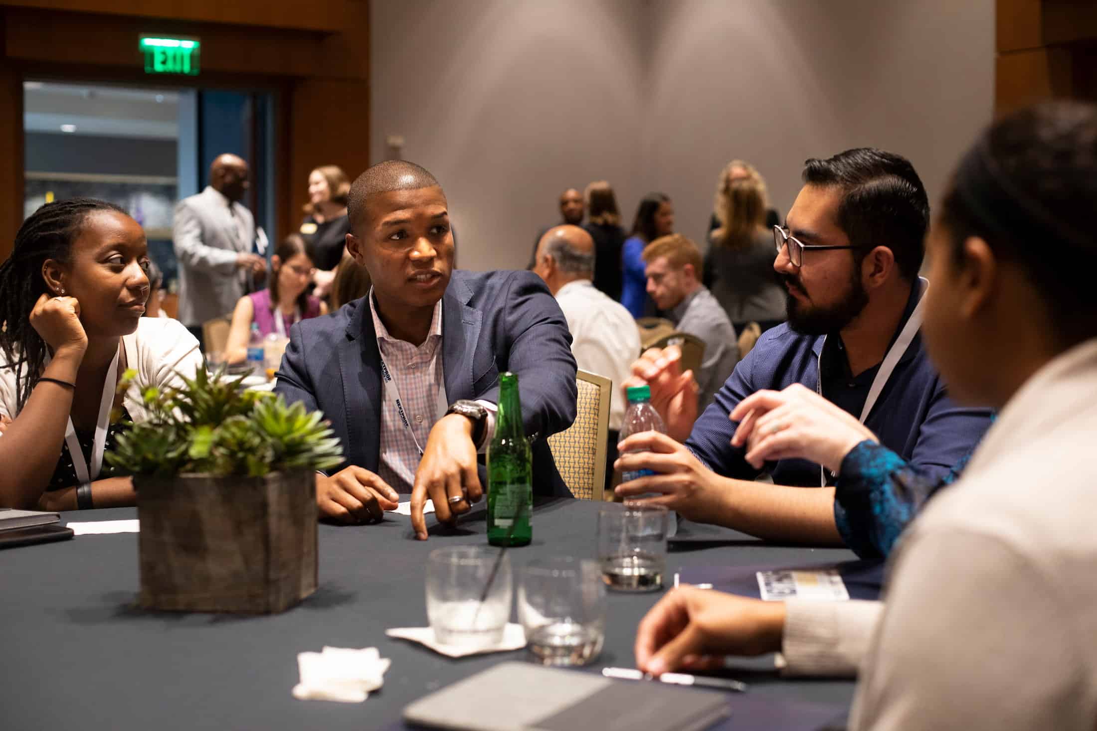 Black man points toward tabletop while talking to other men at a table
